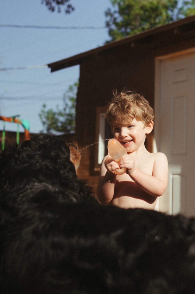 Little boy laughing and squirting water into his dog's mouth. 